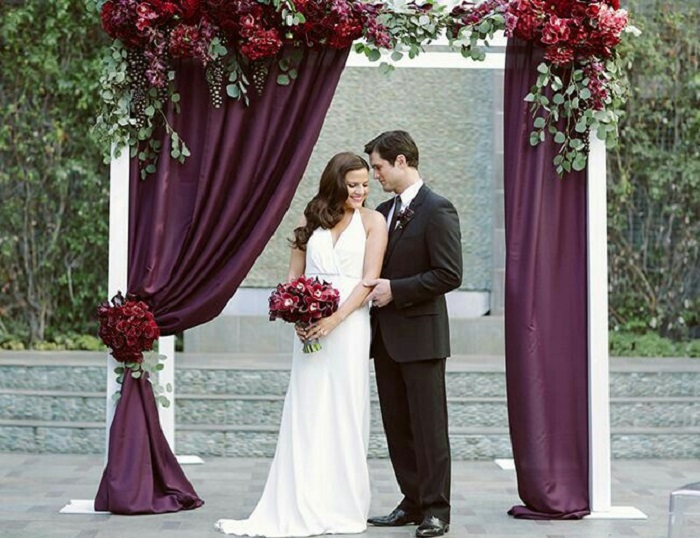wedding altar with burgundy drapes decorated with beautiful seasonal flowers